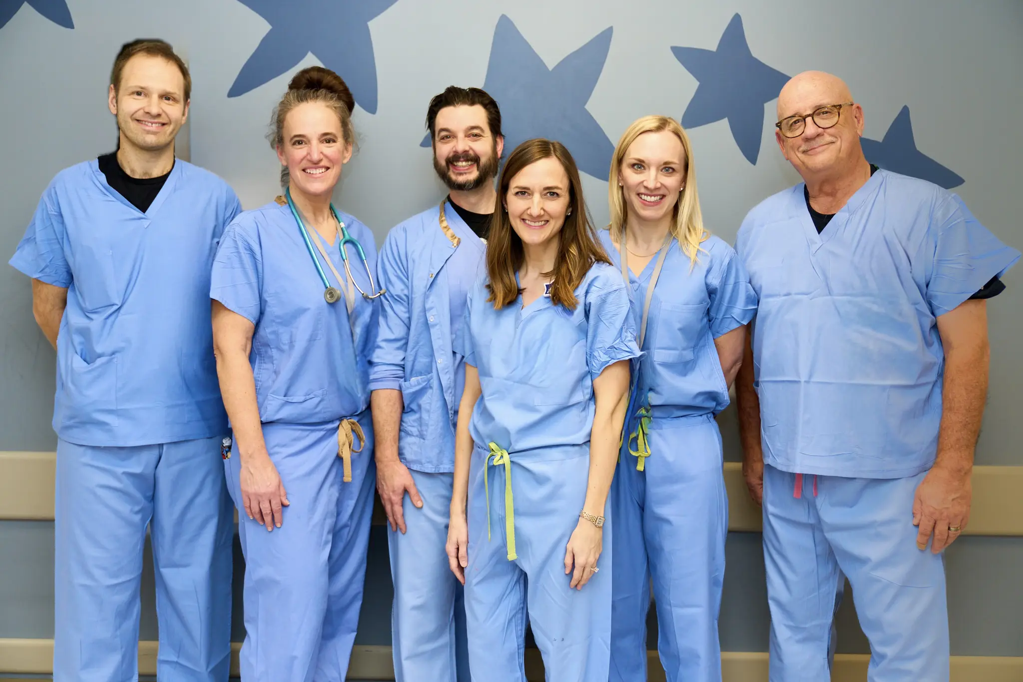 Group of five healthcare professionals in blue scrubs smiling at the camera.