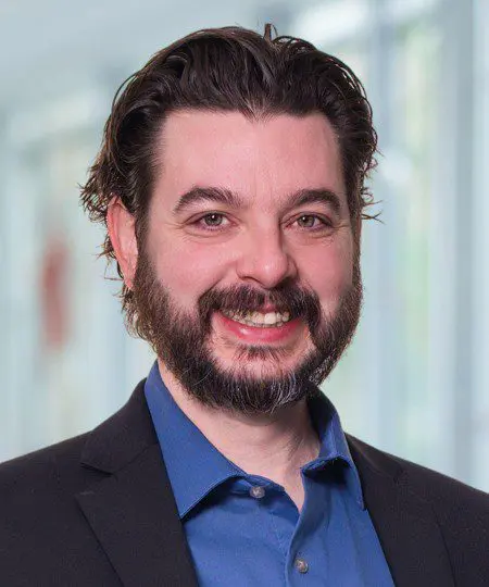 Smiling man with dark hair and beard in a professional setting.