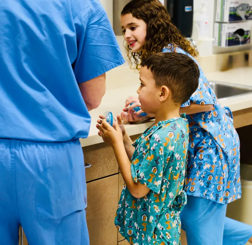 A child in hospital gown talks to a nurse while a woman watches.