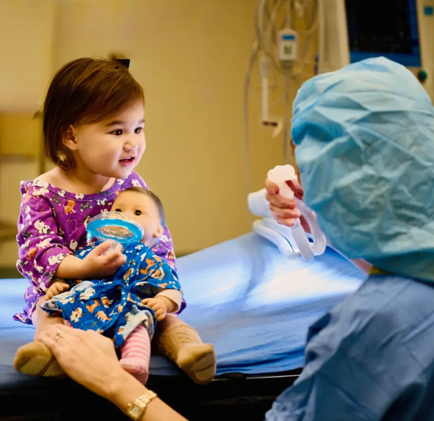 A child with a doll interacts with a person in medical scrubs.